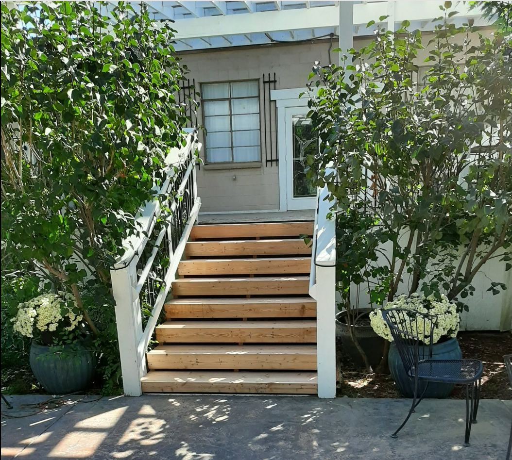Wooden deck steps leading to a light blue door flanked by climbing vines and potted white flowers