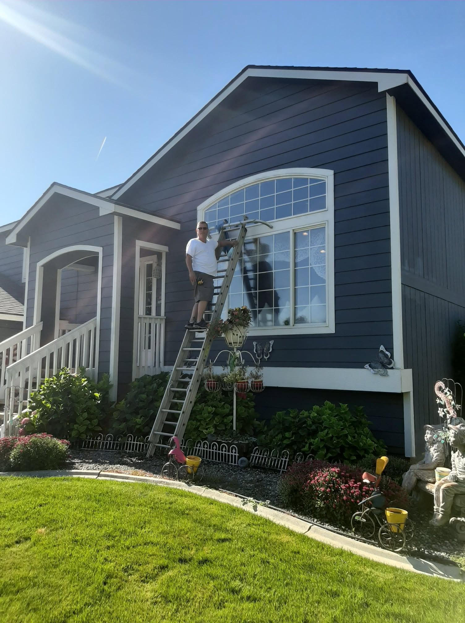 Man on ladder cleaning large arched window on dark blue house with white trim