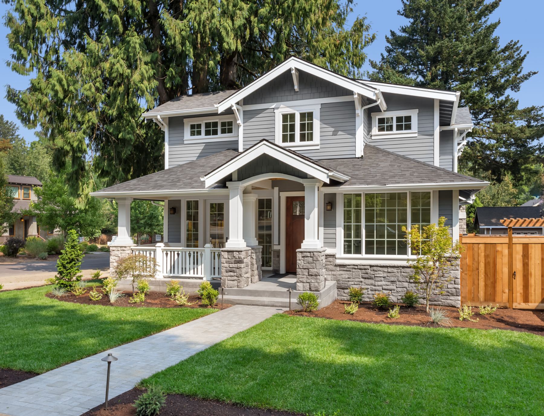 Modern two-story gray and white house with stone porch, columns, and manicured front lawn