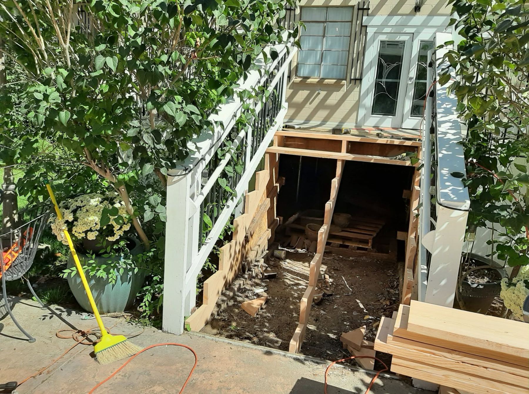 Under-deck construction with wooden framing, climbing vines on railings, and house exterior visible