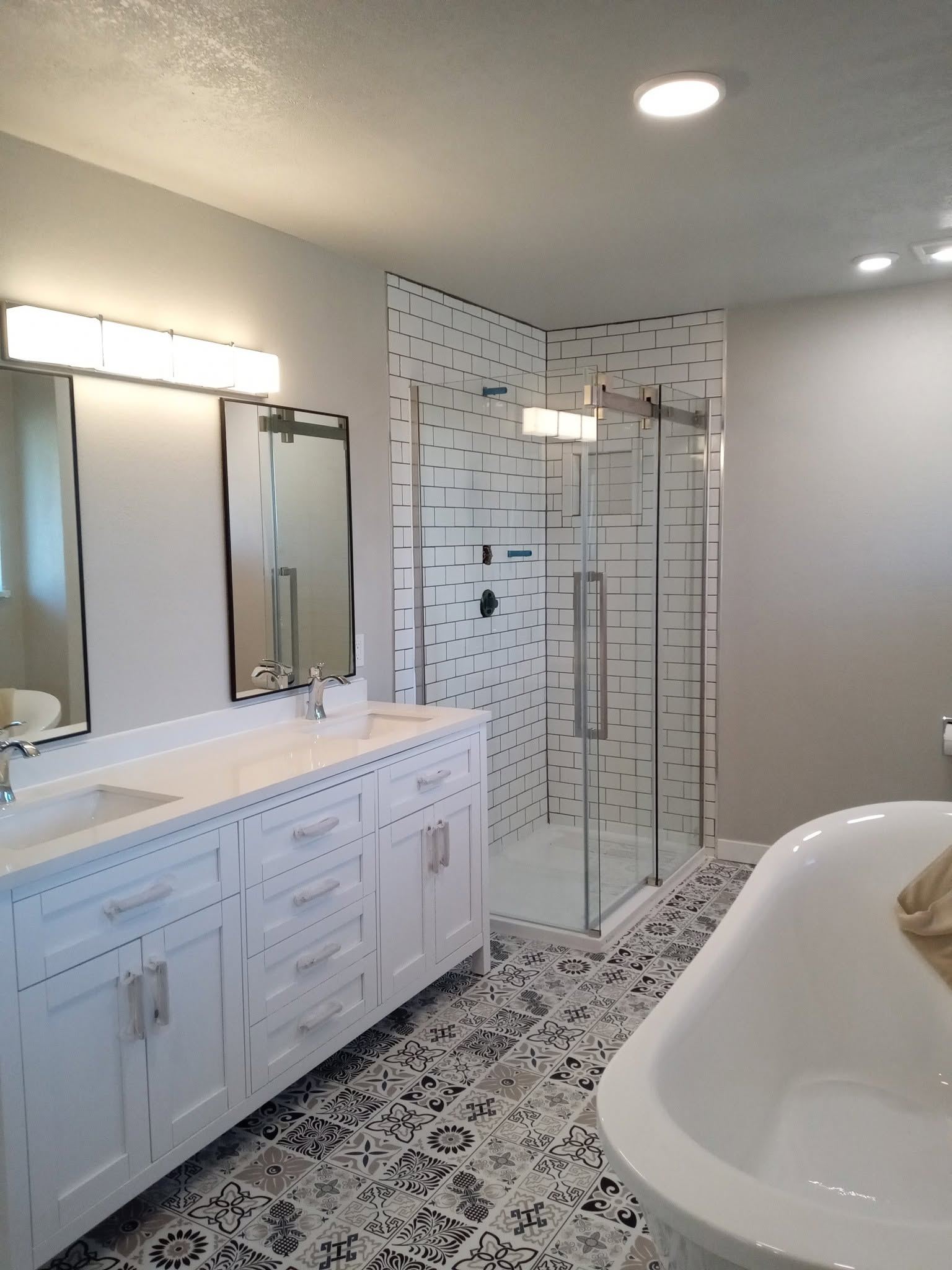 Modern white bathroom with subway tile shower, dual vanity, freestanding tub, and patterned floor tiles