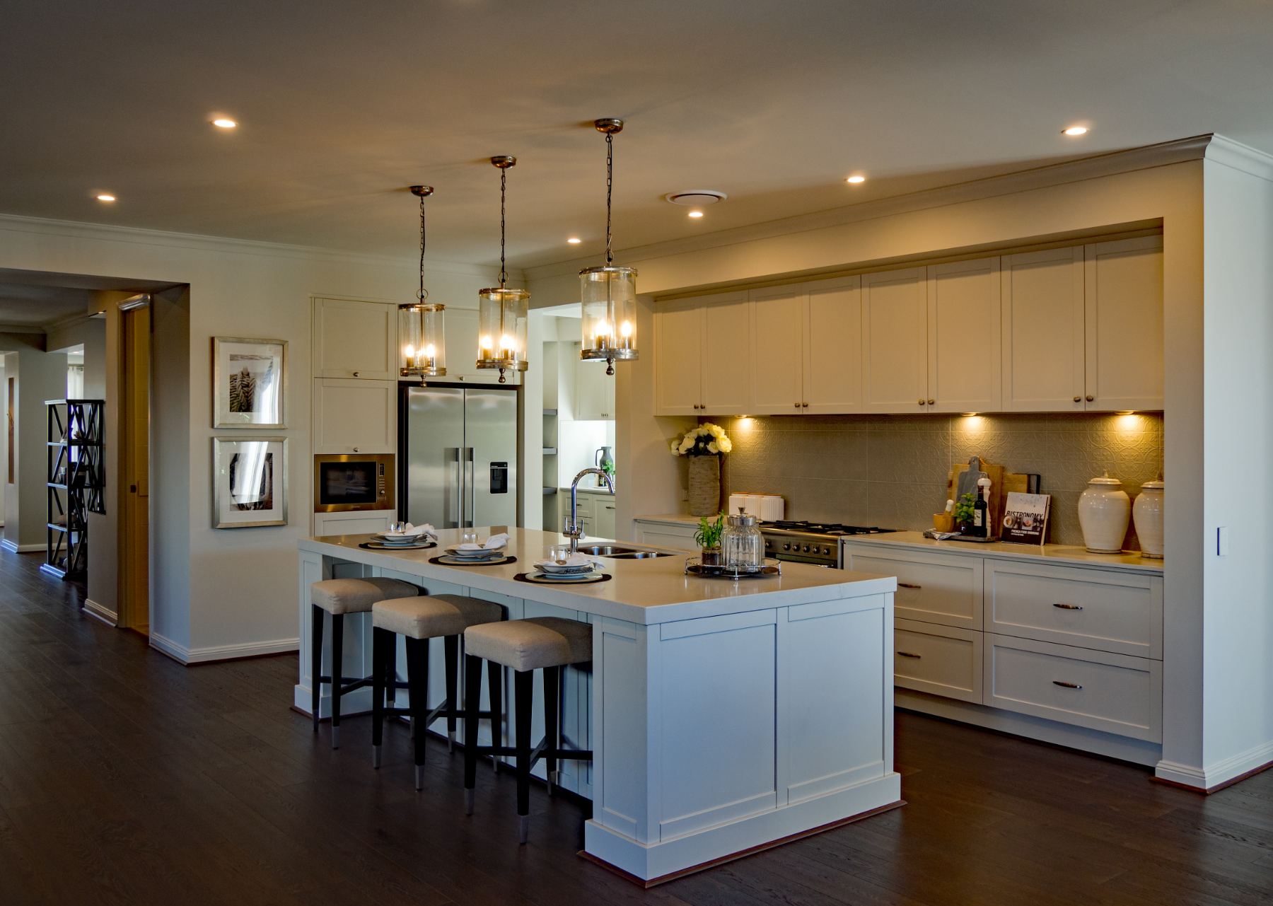 Modern white kitchen with island, pendant lights, stainless steel appliances and dark wood flooring