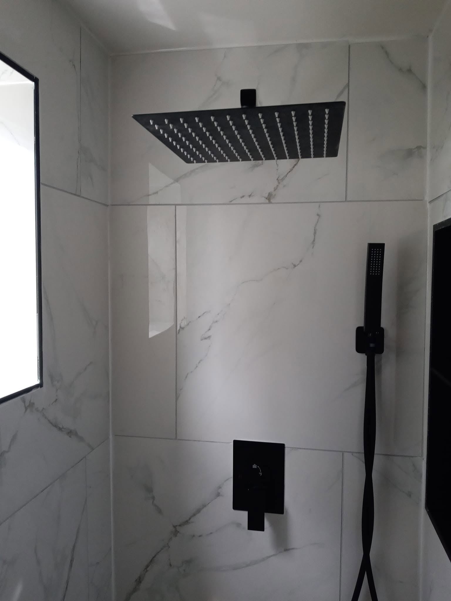 Modern bathroom shower with marble tile walls and black rainfall showerhead fixtures