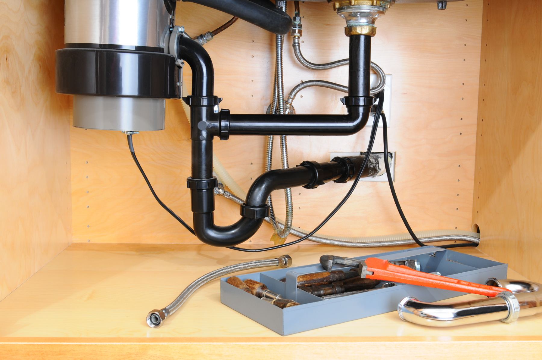 Under-sink plumbing pipes and tools in cabinet with toolbox and wrench